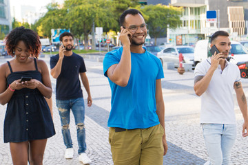 Happy Latin man talking on cell while walking down city street. Mix raced men and women going outside, talking on cells, using mobile phones. Smartphone using concept