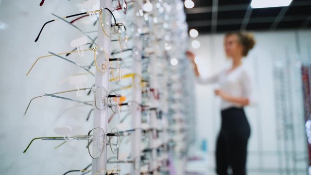 Stand with glasses in the store of optics. Beautiful girl in glasses on a background. Eyesight correction. Optics