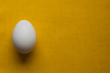 white chicken egg on a bright yellow orange tablecloth. Design for poultry industry, production of eco bio natural food. Free space for text. minimalistic top view. design for banners, cards.