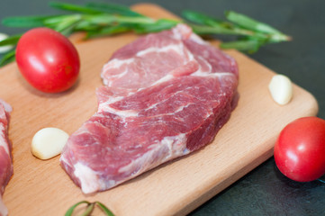 Raw juicy pork steak with red tomatoes, rosemary and garlic on a cutting board.
