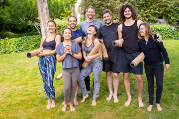 Happy yoga group with mats in park. Cheerful young men and women in sportswear holding yoga mats and smiling at camera in park. Yoga concept