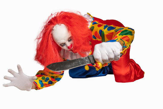 a bad clown lies on the ground and holds a knife in the camera