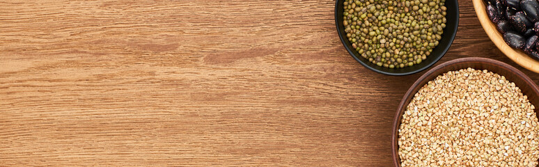 panoramic shot of bowls with raw buckwheat and green moong beans on wooden surface