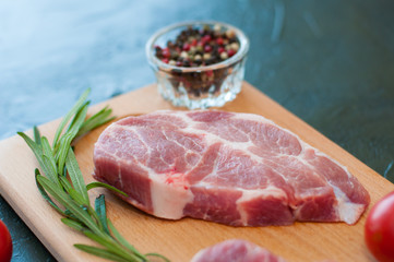 Raw pork steak, rosemary and tomato on cutting board, on dark gray concrete background, close up