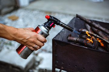Lighter with pistol with gas cartridge. A girl lights the fire in the barbecue with wood.