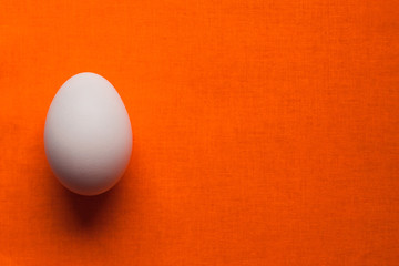 white chicken egg on a bright  orange table cloth. Design for poultry industry, production of eco bio natural food. Free space for text. minimalistic top view. design for banners, cards.