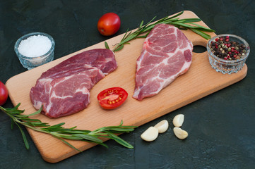 Pork, raw steaks and spices, garlic, salt, pepper, tomatoes and rosemary on cutting board