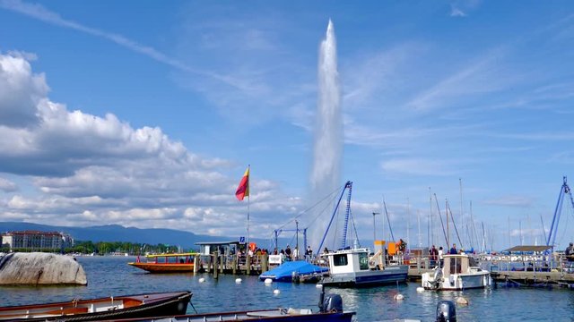 Lake Geneva (Switzerland) in the foreground a small port with several small boats and the water jet behind it in slow mo.