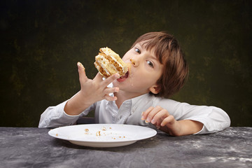 Little boy eating a cake while sitting at the table