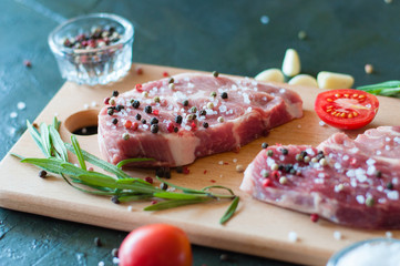 Raw pork meat sprinkled with pepper and salt with chopped tomato garlic and rosemary, steak cooking process