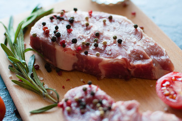 Raw pork meat sprinkled with pepper and salt with chopped tomato and rosemary steak cooking process