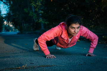 Girl runner doing push ups on sunset in autumn forest and park wearing pink jacket. Young woman...