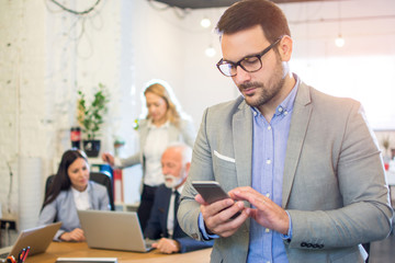 Handsome young businessman wearing formal-wear and eyeglasses using phone in office