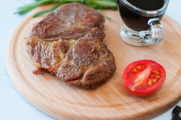 Cooked, grilled pork steak on a wooden round board, with soy sauce, rosemary and tomato