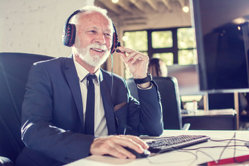 Senior sales agent with headset working on computer in office