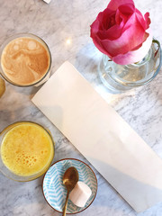 A top view table with a blank menu and drinks in a Cafe, cappuccino and orange juice, sweets and a pink rose