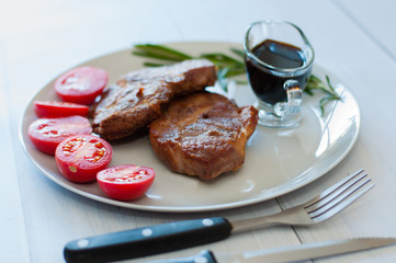 Fried, very tasty and juicy meat steaks of pork or beef with sauce, spices and tomatoes, on a gray plate, on light wooden background