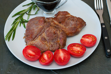 Juicy meat steaks with rosemary, sauce, tomatoes on a plate, on dark gray concrete background