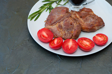Fragrant pork steaks with spices, tomatoes and sauce, on a gray plate, on dark background with place for text