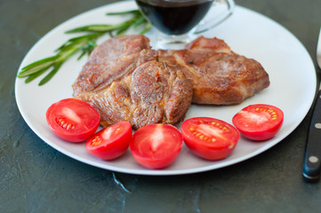 Fragrant pork meat steaks with spices, tomatoes and sauce, on a gray plate, on dark concrete background with place for text