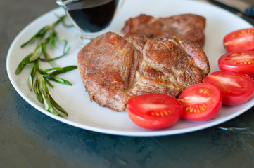 Fragrant, juicy pork meat steaks with rosemary, tomatoes and sauce, on gray plate, close-up