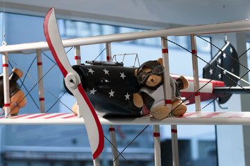 Teddy bear in pilot's glasses and pilot's jacket on the wing of an old airplane. storefront.