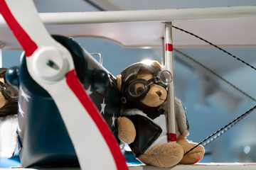 Teddy bear wearing pilot glasses and a pilot's jacket on the wing of a vintage aircraft. close up.