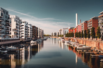 Modern luxury home buildings at the riverside with a marina view with small boats on a bright sunny blue sky day. Water view from the flat. Marina Westhafen, Frankfurt am Main, Germany - obrazy, fototapety, plakaty