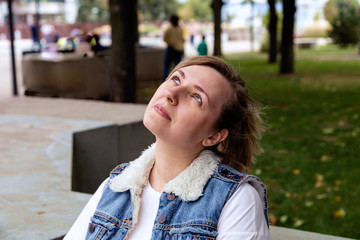 Closeup portrait of a young girl with blond hair and in a denim vest for a walk in a city park on a summer afternoon.