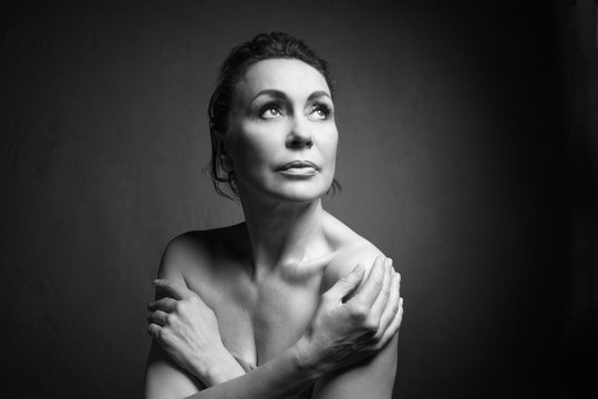 Portrait of a sensual fifty year old woman on grey studio background. Monochrome shot.