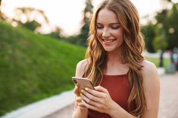 Ginger woman walking in park outdoors using mobile phone.