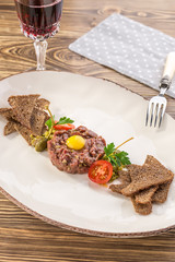Steak Tartare with rye bread toasts and yolk on top and glass of red wine on wooden table