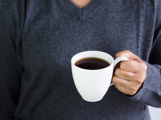 woman in gray sweater holding a white cup of black coffee, concept of warming up the drink in cold.