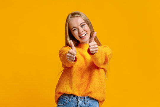 Joyful teenage girl showing thumbs up on orange background