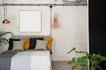 Modern interior of bedroom in loft apartment with double bed and white brick wall with frame with mock up. Industrial and scandinavian style.