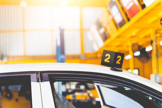 The white luxury vehicle is parked waiting for repair or inspection of maintenance at the garage. There are queue numbers on the car roof in transportation and engineering concept.
