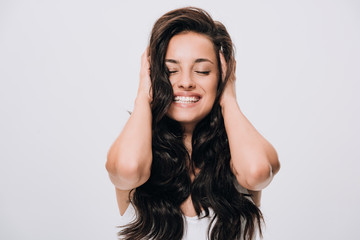 happy brunette beautiful woman touching long curly healthy hair isolated on grey