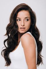 brunette beautiful woman with long curly healthy hair looking away isolated on grey