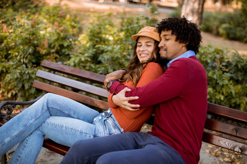 Multiratial loving couple sitting on bench in the autumn city park