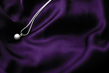 Luxury white gold pearl necklace on dark violet silk background, holiday glamour jewelery present