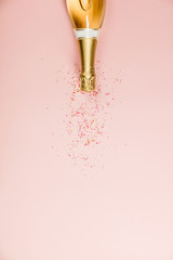 Flat lay of Celebration. Champagne bottle with sprinkles on pink background.
