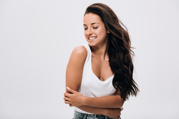 smiling brunette beautiful woman with crossed arms and long healthy and shiny hair isolated on grey