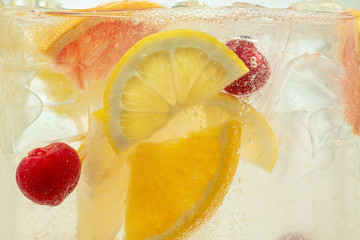 Close up of lemon slices and cherry in lemonade and ice cubes background. Texture of cooling sweet summer's drink with macro bubbles on the glass wall. Fizzing or floating up to top of surface.