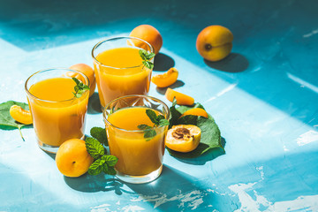Glass of fresh healthy apricot juice in sunny light on blue surface