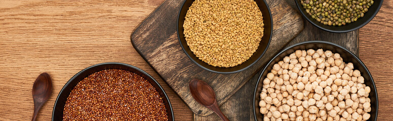 panoramic shot of bowls with buckwheat, beans and chickpea near wooden spoons on cutting boards