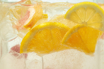 Close up of lemon slices and cherry in lemonade and ice cubes background. Texture of cooling sweet summer's drink with macro bubbles on the glass wall. Fizzing or floating up to top of surface.