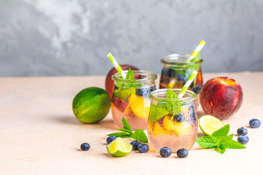 Blueberry and peach infused water, cocktail, lemonade or tea. Summer iced cold drink with blueberry, lime, peach and mint