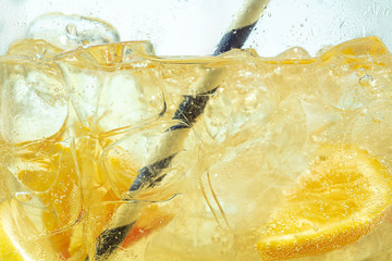 Close up of lemon slices in stirring the lemonade and ice cubes on background. Texture of cooling sweet summer's drink with macro bubbles on the glass wall. Fizzing or floating up to top of surface. - obrazy, fototapety, plakaty