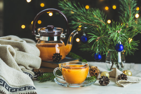 Christmas and New Year composition. Cup and teapot of hot spicy tea with sea buckthorn, jam in the glass jar, branches of pine and spruce, holiday decor, bokeh