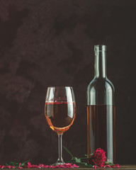 Bottle of rose wine and glass served with rose wine and rose petals, pink rose on dark background